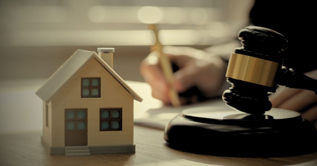 Small commercial property model next to a judge’s gavel on a desk, symbolizing business insurance coverage.