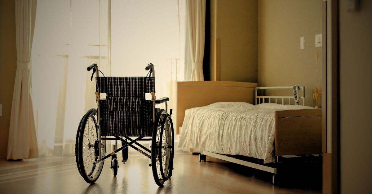 Empty wheelchair next to a hospital-style bed in a nursing home room.