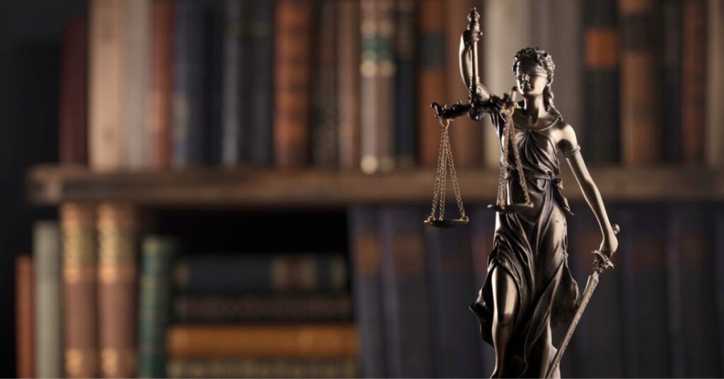 Statue of Lady Justice holding scales and a sword in front of a bookshelf.
