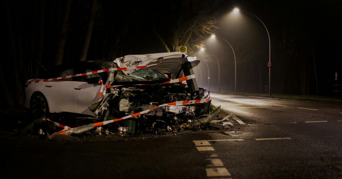 Severely damaged car after a nighttime crash on a city road, surrounded by police tape.