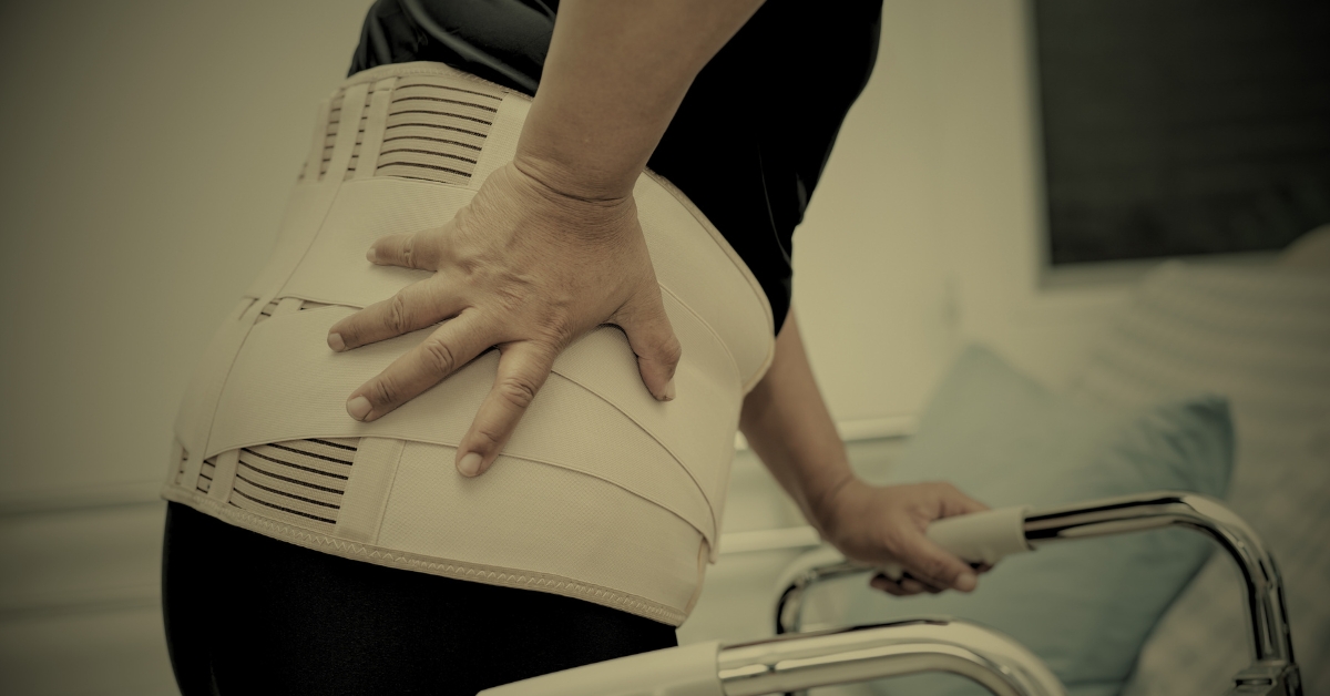 Adult wearing a lumbar back brace and holding a walker, illustrating recovery after a spinal cord injury.